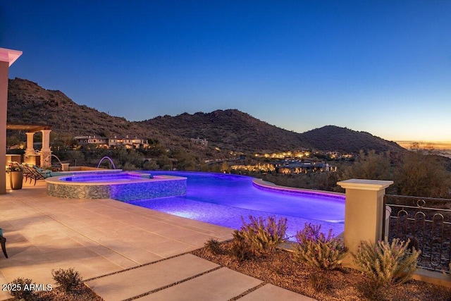 pool at dusk with an in ground hot tub, a mountain view, pool water feature, and a patio area