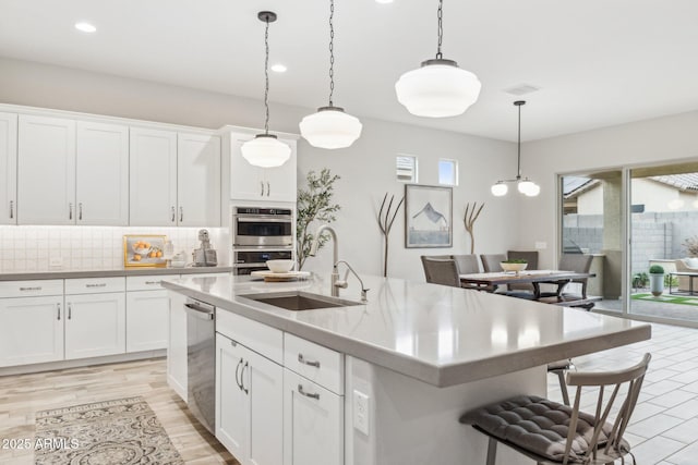 kitchen featuring tasteful backsplash, an island with sink, decorative light fixtures, a kitchen bar, and a sink