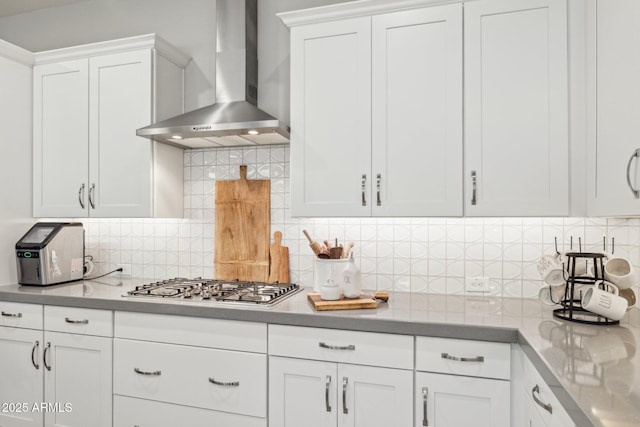 kitchen with wall chimney exhaust hood, stainless steel gas cooktop, white cabinets, and backsplash
