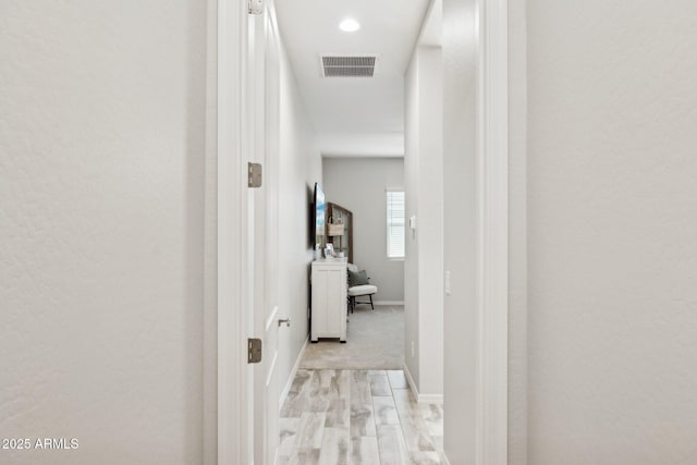 corridor with light wood finished floors, visible vents, and baseboards