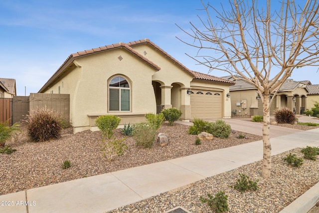 mediterranean / spanish home featuring a garage, concrete driveway, a tiled roof, fence, and stucco siding