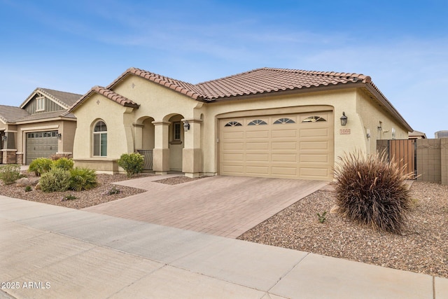 mediterranean / spanish home with an attached garage, a tiled roof, decorative driveway, and stucco siding