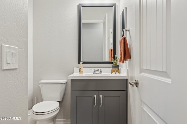 half bathroom with a textured wall, vanity, and toilet