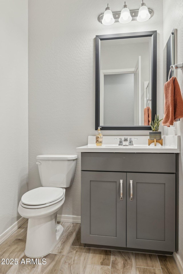 bathroom featuring toilet, baseboards, wood finished floors, and vanity