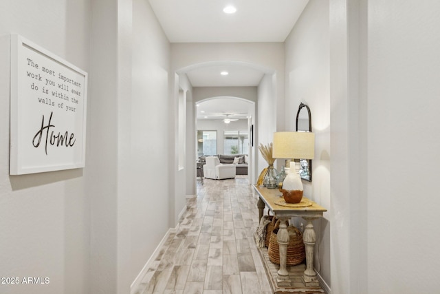 hall featuring light wood-style floors, arched walkways, baseboards, and recessed lighting