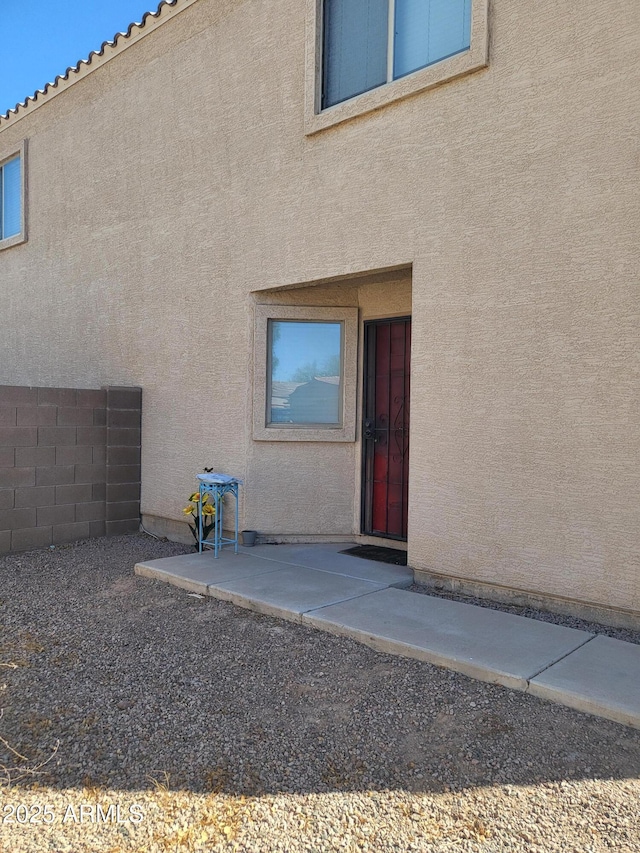 entrance to property featuring a patio area, fence, and stucco siding