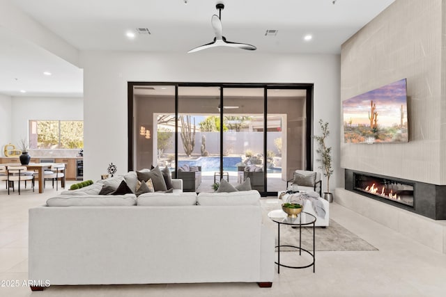 tiled living room with a tiled fireplace, ceiling fan, and a healthy amount of sunlight