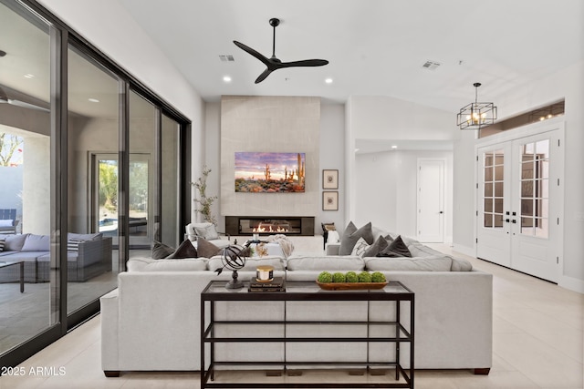 living room featuring vaulted ceiling, a large fireplace, french doors, and ceiling fan with notable chandelier