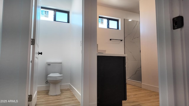 bathroom featuring healthy amount of natural light, toilet, wood finished floors, and baseboards