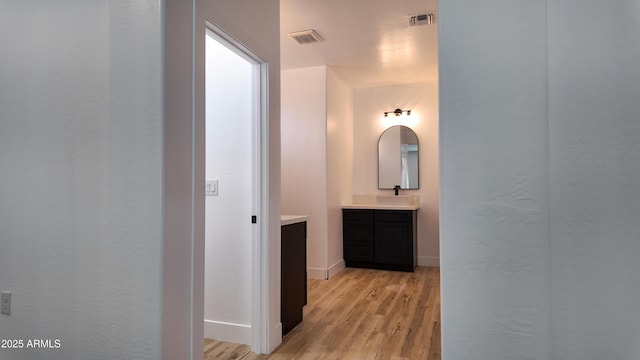 hall with light wood-style floors, a sink, and baseboards