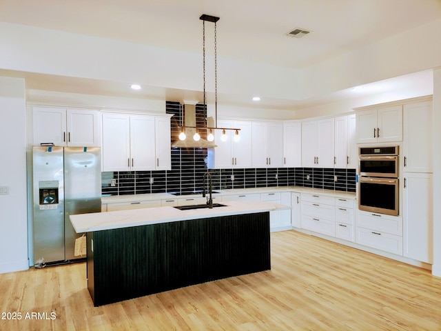 kitchen featuring stainless steel appliances, an island with sink, hanging light fixtures, and white cabinets