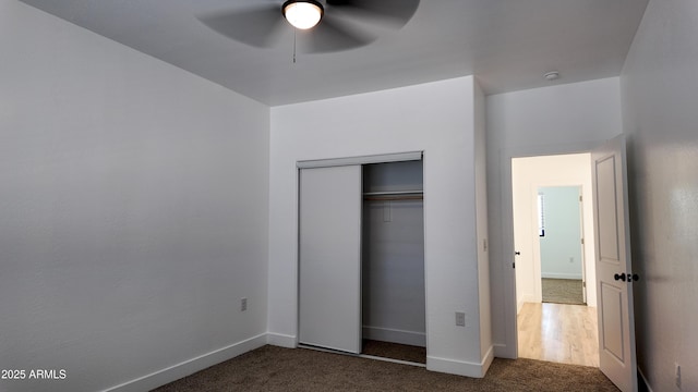 unfurnished bedroom featuring dark carpet, baseboards, a closet, and a ceiling fan