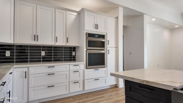 kitchen featuring stainless steel double oven, tasteful backsplash, light stone counters, light wood-type flooring, and recessed lighting