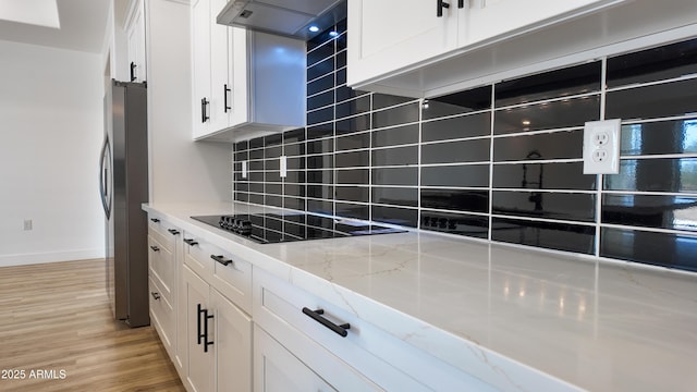 kitchen featuring black electric stovetop, freestanding refrigerator, white cabinetry, decorative backsplash, and extractor fan