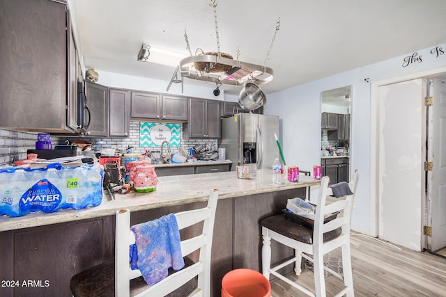 kitchen featuring stainless steel fridge, light wood-type flooring, backsplash, dark brown cabinetry, and kitchen peninsula