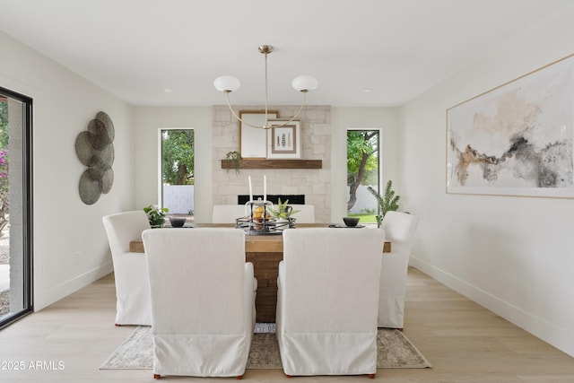 dining room featuring light wood-type flooring, a fireplace, and baseboards