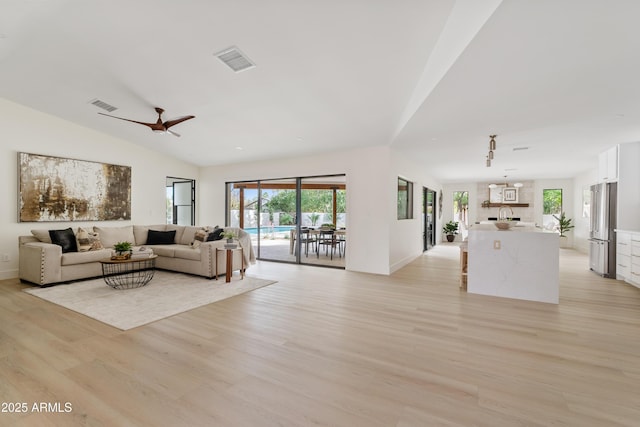 living area with visible vents, vaulted ceiling, light wood-style flooring, and ceiling fan