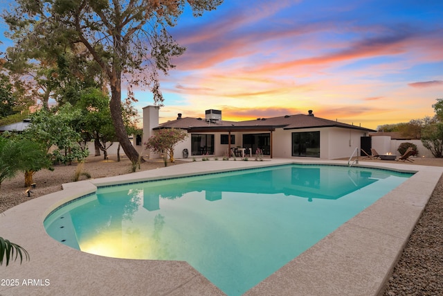 pool at dusk with a patio area, fence, and a fenced in pool