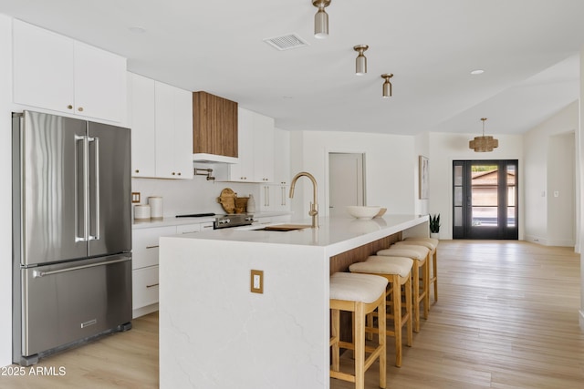 kitchen with a breakfast bar, high end refrigerator, a sink, visible vents, and light wood-type flooring