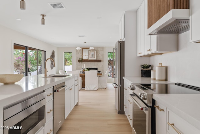 kitchen with a sink, visible vents, light countertops, appliances with stainless steel finishes, and range hood