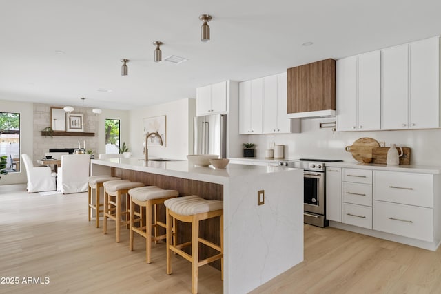 kitchen featuring a kitchen island with sink, a sink, light countertops, appliances with stainless steel finishes, and light wood-type flooring