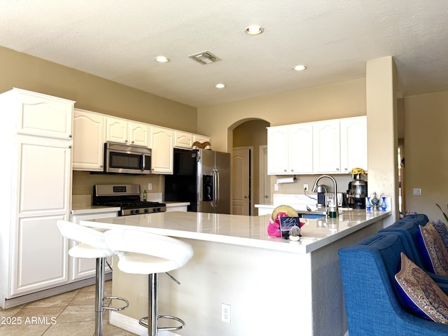 kitchen featuring white cabinetry, a kitchen bar, light tile patterned floors, kitchen peninsula, and stainless steel appliances