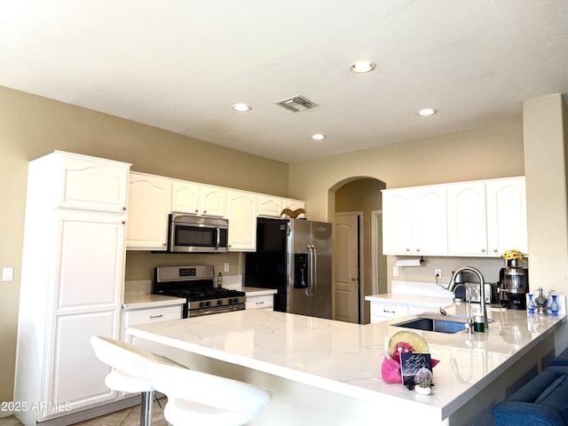 kitchen with appliances with stainless steel finishes, sink, a kitchen bar, kitchen peninsula, and light stone countertops