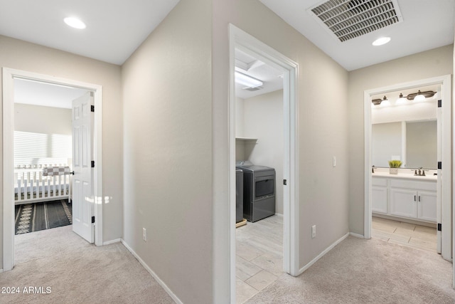 hall with light carpet, sink, and independent washer and dryer