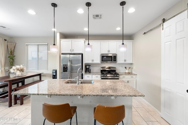 kitchen featuring a barn door, an island with sink, stainless steel appliances, pendant lighting, and sink