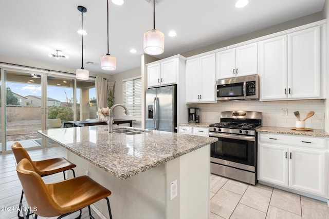 kitchen with decorative light fixtures, sink, white cabinetry, a kitchen island with sink, and stainless steel appliances