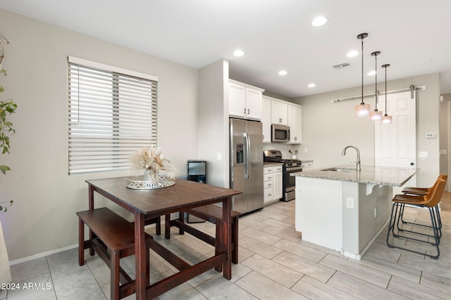 kitchen with light stone countertops, appliances with stainless steel finishes, decorative light fixtures, white cabinetry, and sink