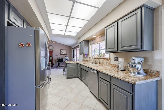 kitchen with appliances with stainless steel finishes, light stone counters, gray cabinetry, sink, and lofted ceiling