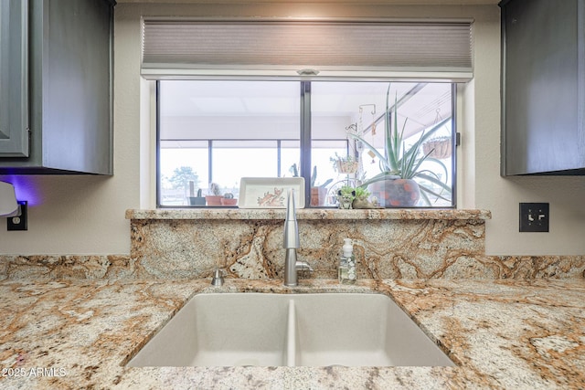 kitchen featuring gray cabinets, light stone counters, and sink