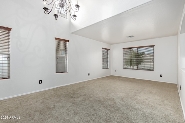 empty room featuring carpet flooring, a wealth of natural light, and a notable chandelier