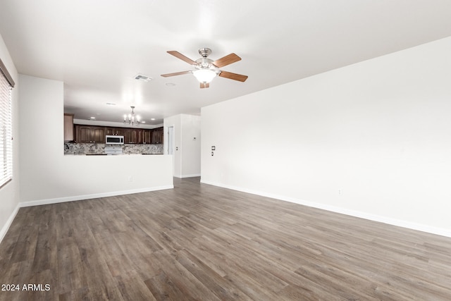 unfurnished living room featuring ceiling fan with notable chandelier and dark wood-type flooring