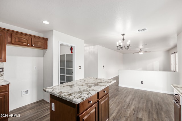 kitchen with pendant lighting, a center island, ceiling fan with notable chandelier, light stone countertops, and dark hardwood / wood-style flooring