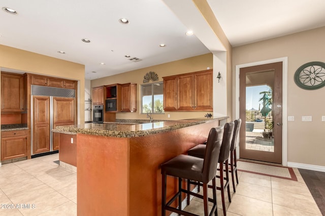 9753 E Suncrest Rd, Scottsdale, AZ 85262 - kitchen featuring brown cabinetry, black appliances, light tile patterned floors, a kitchen breakfast bar, and recessed lighting