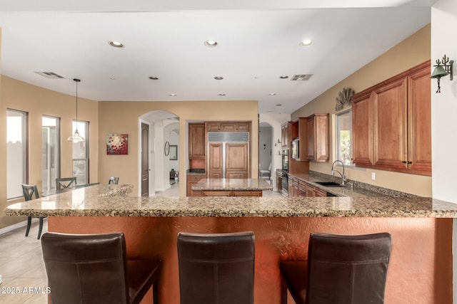 9753 E Suncrest Rd, Scottsdale, AZ 85262 - kitchen with paneled built in refrigerator, a sink, brown cabinetry, arched walkways, and light stone countertops