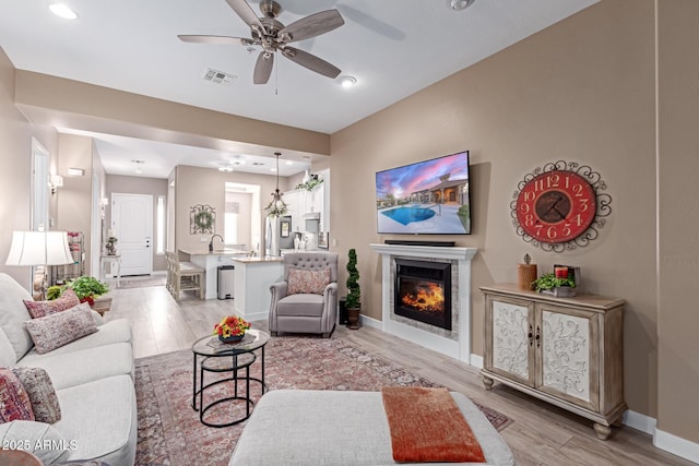 living area with baseboards, visible vents, ceiling fan, a glass covered fireplace, and light wood-type flooring