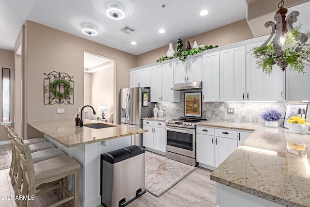 kitchen featuring visible vents, a kitchen bar, under cabinet range hood, a sink, and appliances with stainless steel finishes