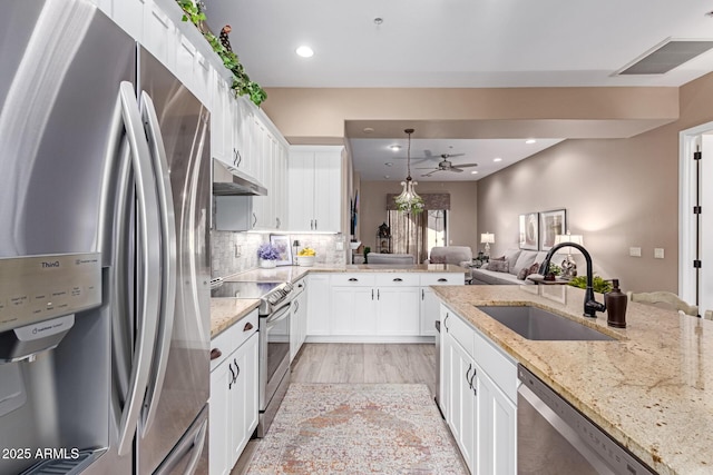 kitchen with a sink, decorative backsplash, stainless steel appliances, white cabinets, and under cabinet range hood