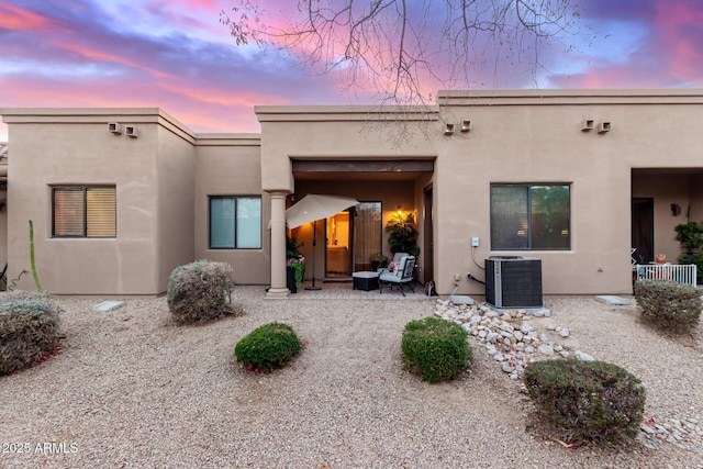 back of property at dusk featuring central AC unit and stucco siding