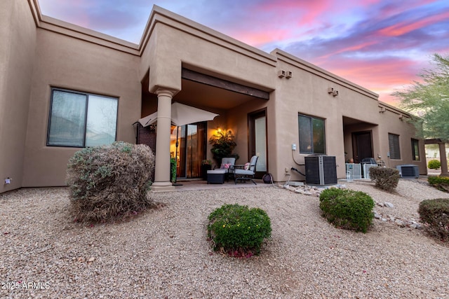 back of house at dusk featuring cooling unit and stucco siding