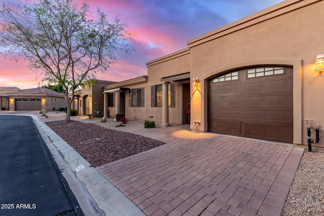 view of front facade with a tile roof, decorative driveway, a garage, and stucco siding