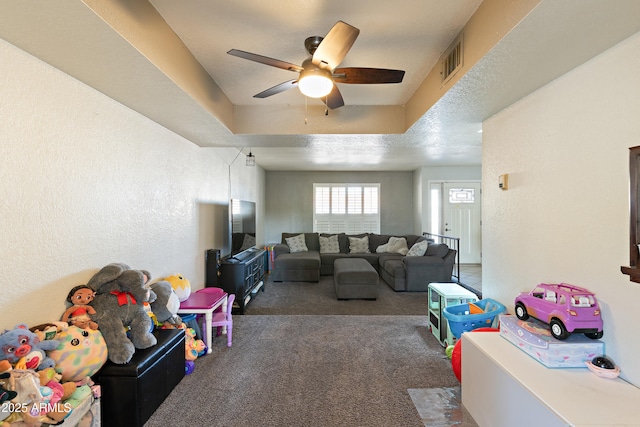 playroom with ceiling fan, a tray ceiling, and dark carpet