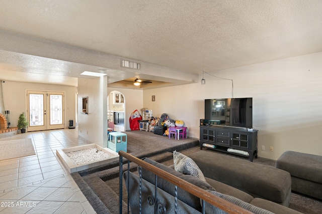 tiled living room featuring ceiling fan, french doors, and a textured ceiling