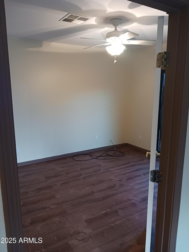 empty room with dark wood-type flooring, visible vents, a ceiling fan, and baseboards