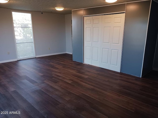 unfurnished bedroom with a closet, a textured ceiling, baseboards, and dark wood finished floors