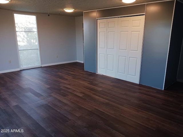 unfurnished bedroom featuring a textured ceiling, dark wood-style flooring, a closet, and baseboards