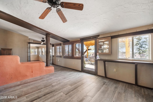 unfurnished living room featuring wood finished floors, ceiling fan, baseboards, a textured ceiling, and beam ceiling